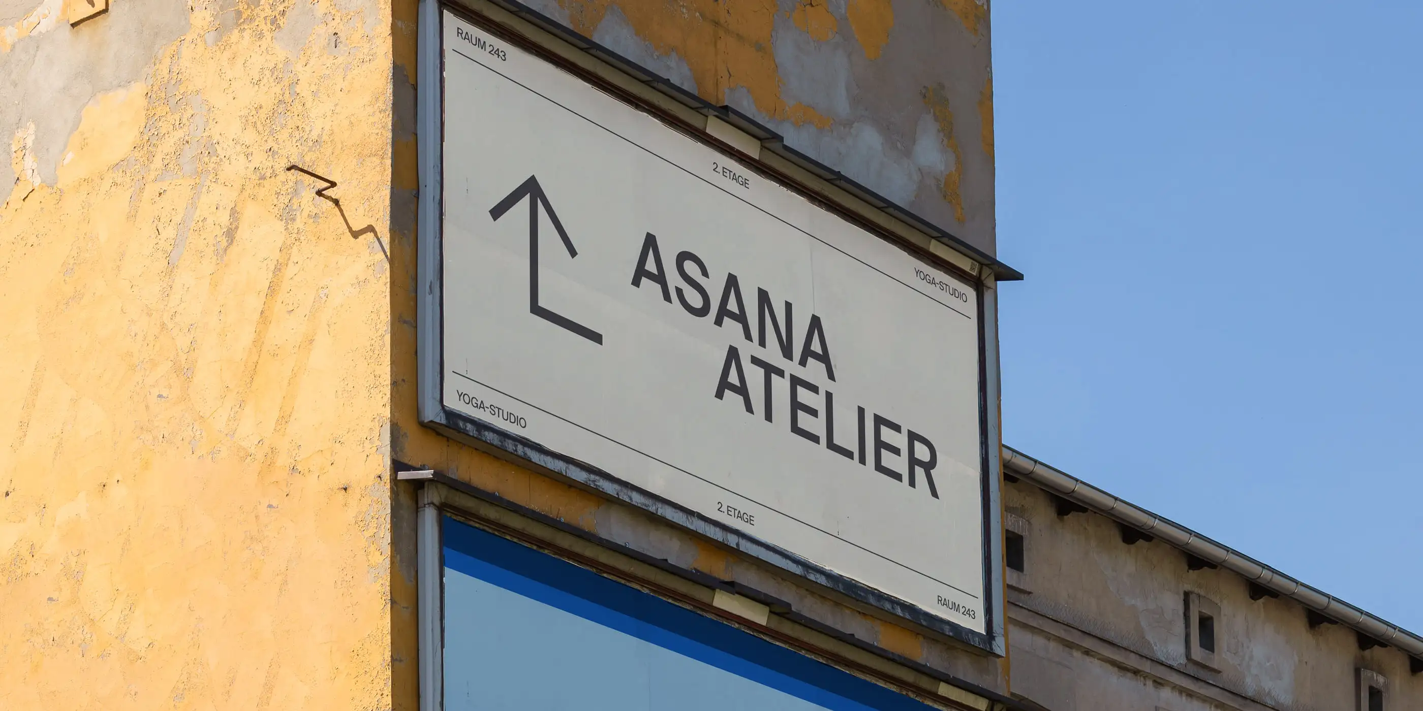 Ein Schild an einem verwitterten gelben Gebäude weist den Weg zum Yoga-Studio Asana Atelier im 2. Stock.