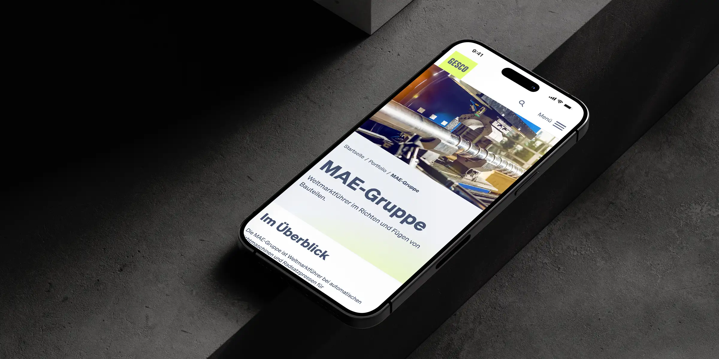 Auf einem Smartphone wird die Gesco Webseite mit der Unterseite der MAE-Gruppe mit einem Bild einer Industriemaschine gezeigt.